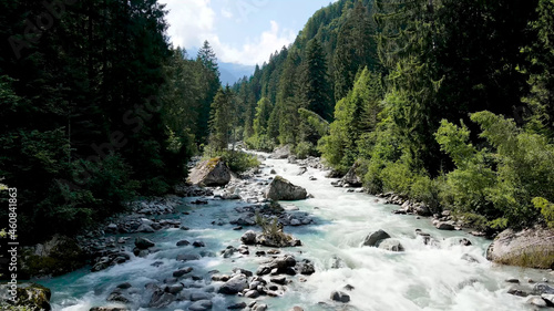 Fast mountain river, large boulders, conifers standing with a wall on the sides