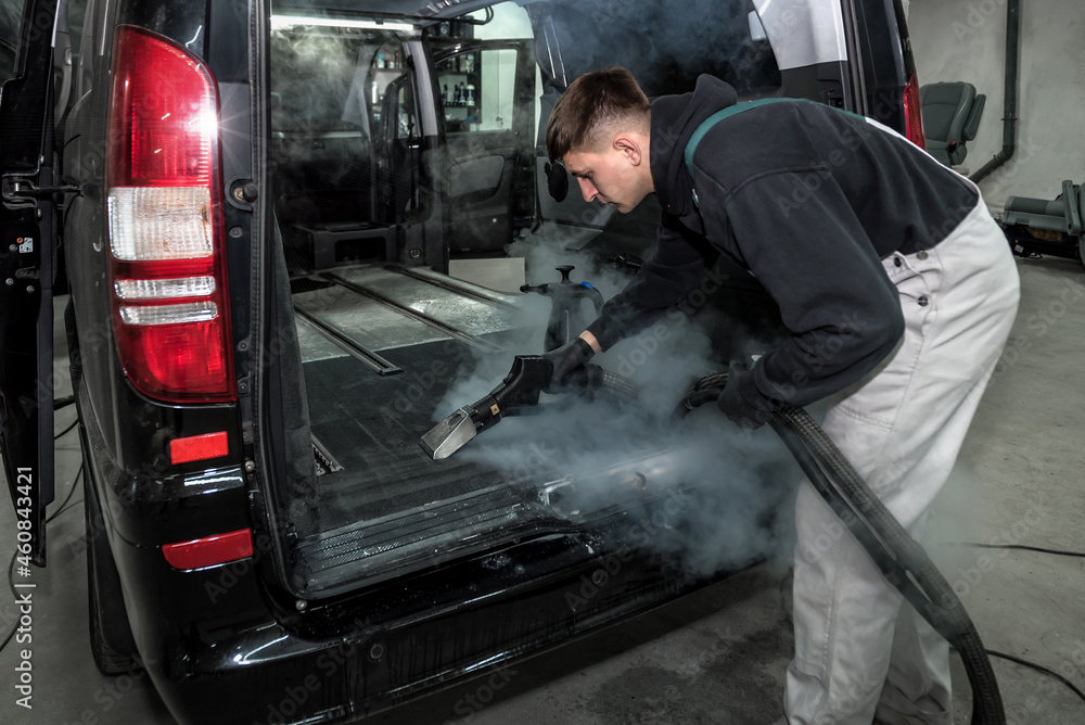Car service worker cleaning car with a steam cleaner