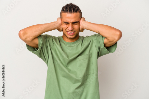 Young venezuelan man isolated on white background covering ears with hands trying not to hear too loud sound.