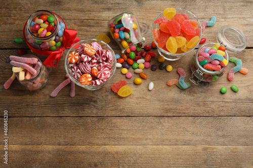 Jars with different delicious candies on wooden table, flat lay. Space for text