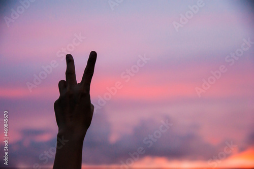 silhouette of a person hand with v shape of sign in the sunset