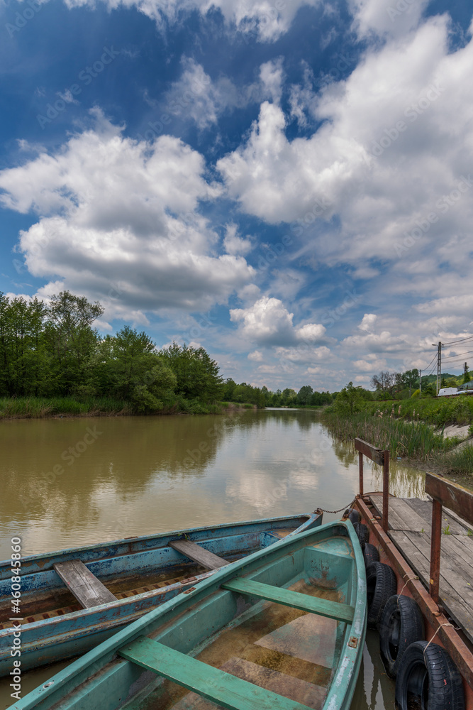 Canoes moored to a jetty on the waters of a river with a blue sky full of clouds