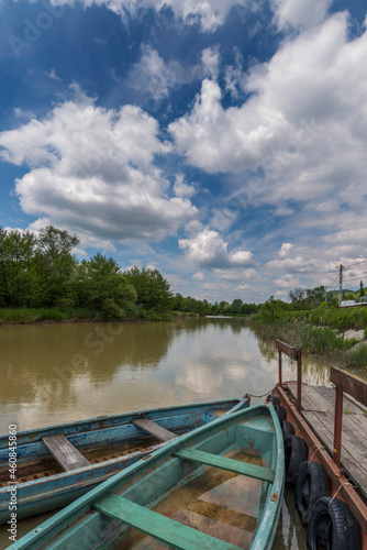 Canoes moored to a jetty on the waters of a river with a blue sky full of clouds