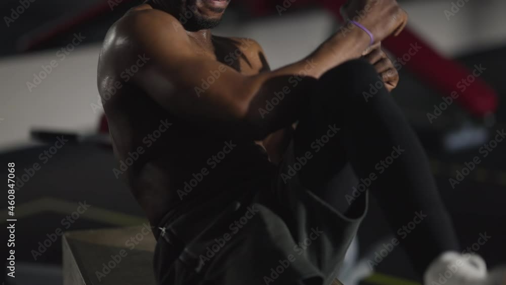 Unrecognizable fit African American sportsman training belly muscles pumping press sitting on gym cube indoors. Motivated strong confident tattooed man exercising. Healthy lifestyle and motivation Unrecognizable fit African American sportsman training belly muscles pumping press sitting on gym cube indoors. Motivated strong confident tattooed man exercising. Healthy lifestyle and motivation