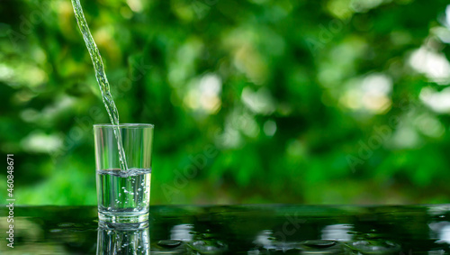 Water flows into a glass placed on a wooden bar. © Jinnawat