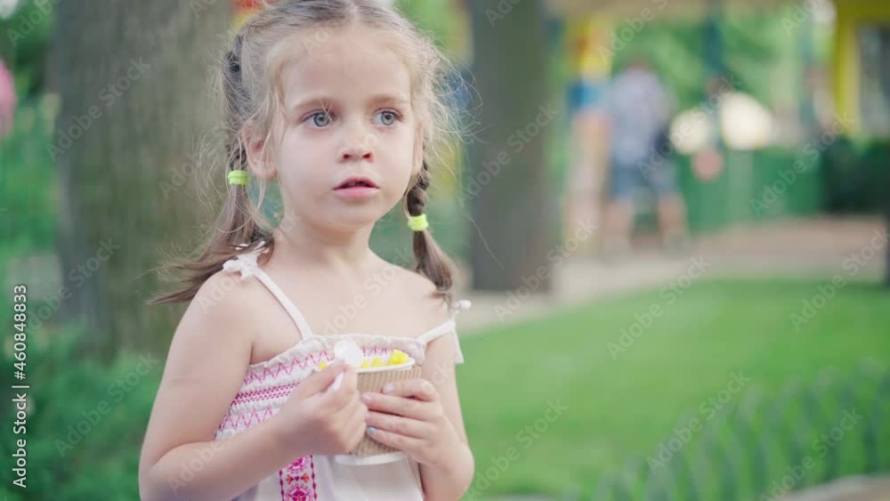 Little girl eat corn paper glass sitting bench summer park Street food concept. Caucasian child enjoy corn grain fast food