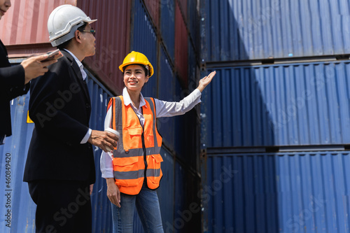 woman worker working with Foreman, standing with ware a yellow helmet to control loading and check a quality of containers from Cargo freight ship for import and export at shipyard or harbor