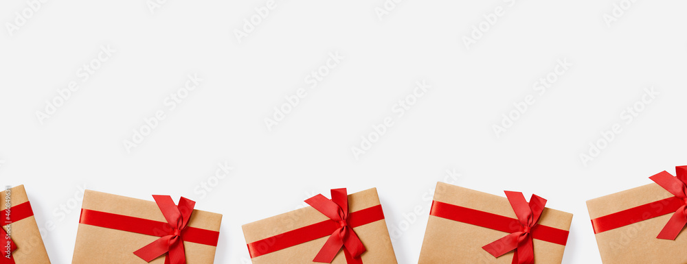 Fototapeta premium Christmas gifts and presents concept web banner with copy space. Gift boxes wrapped in craft paper with red bow on white background.