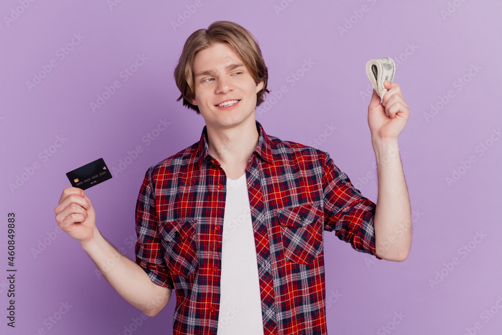 Portrait of positive guy hold credit card cash banknotes decide make choice on purple background Portrait of positive guy hold credit card cash banknotes decide make choice on purple background