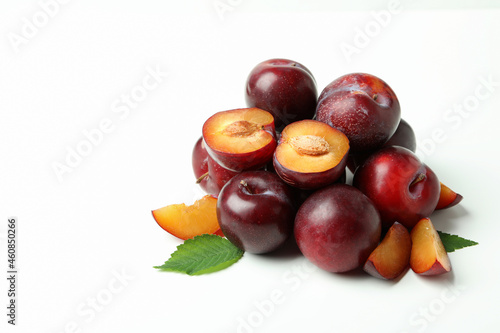 Tasty plums with leaves on white background