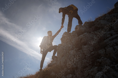 Help and assistance concept. Silhouettes of two people climbing mountains and helping against the blue sky. Walk in the clouds. Discovery Travel Direction Concept