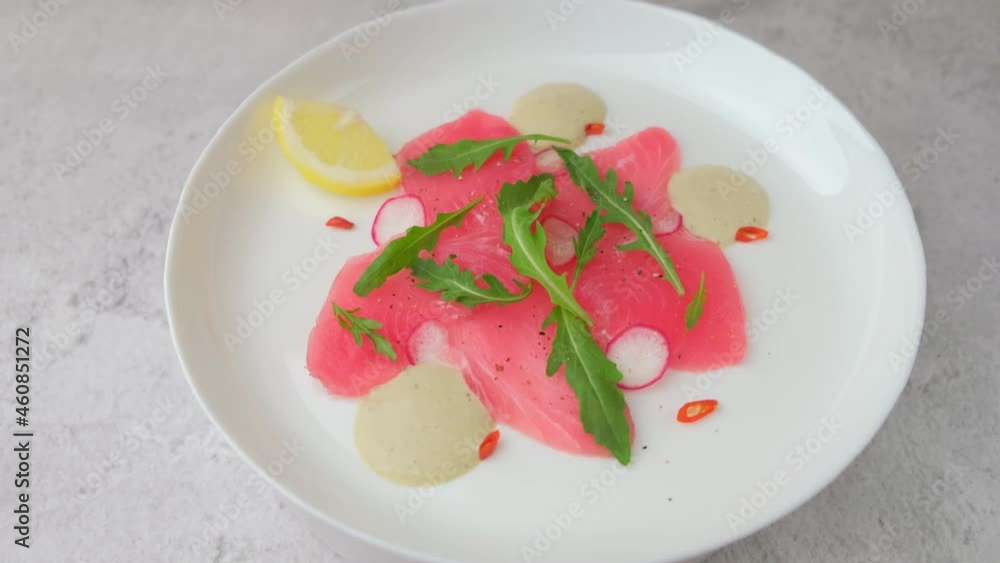 Fresh tuna carpaccio with arugula, radish, chili and lemon. Traditional cold appetizer of Italian cuisine. Close-up, selective focus, rotation. Fresh tuna carpaccio with arugula, radish, chili and lemon. Traditional cold appetizer of Italian cuisine. Close-up, selective focus, rotation.