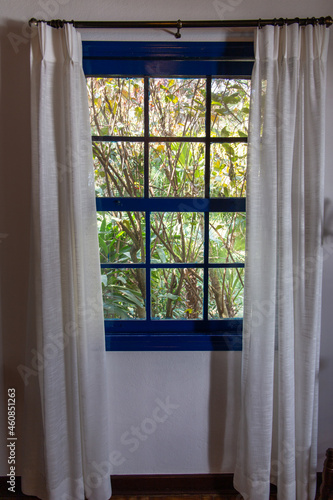 window overlooking nature on a farm in S  o Paulo  Brazil. Blue  old colonial windows. with white curtain