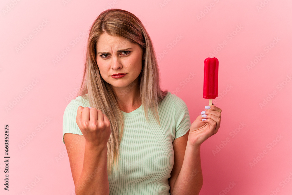 Young russian woman holding an ice cream isolated on pink background showing fist to camera, aggressive facial expression. Young russian woman holding an ice cream isolated on pink background showing fist to camera, aggressive facial expression.
