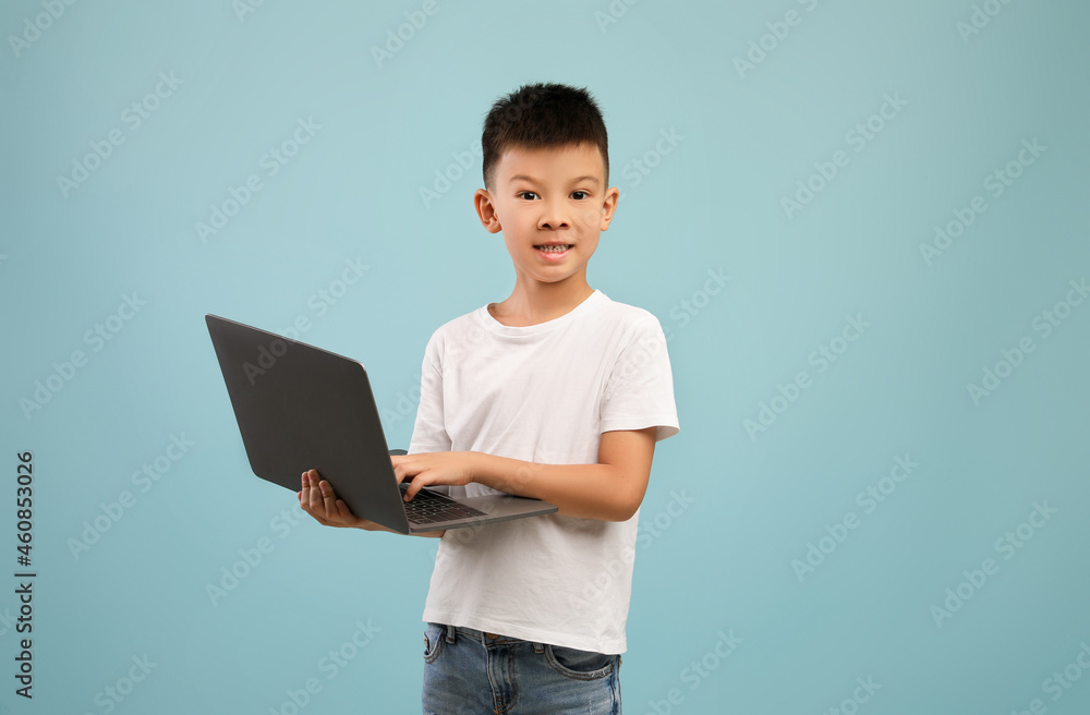 Online Education Concept. Little Asian Boy With Laptop Posing Over Blue Background Online Education Concept. Little Asian Boy With Laptop Posing Over Blue Background