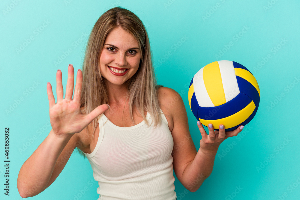 Young russian woman playing volleyball isolated on blue background smiling cheerful showing number five with fingers.