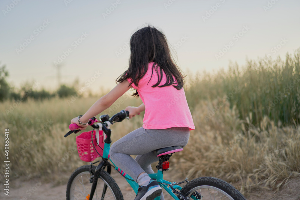 Happy girl riding a bike on a road in the field at sunset Happy girl riding a bike on a road in the field at sunset