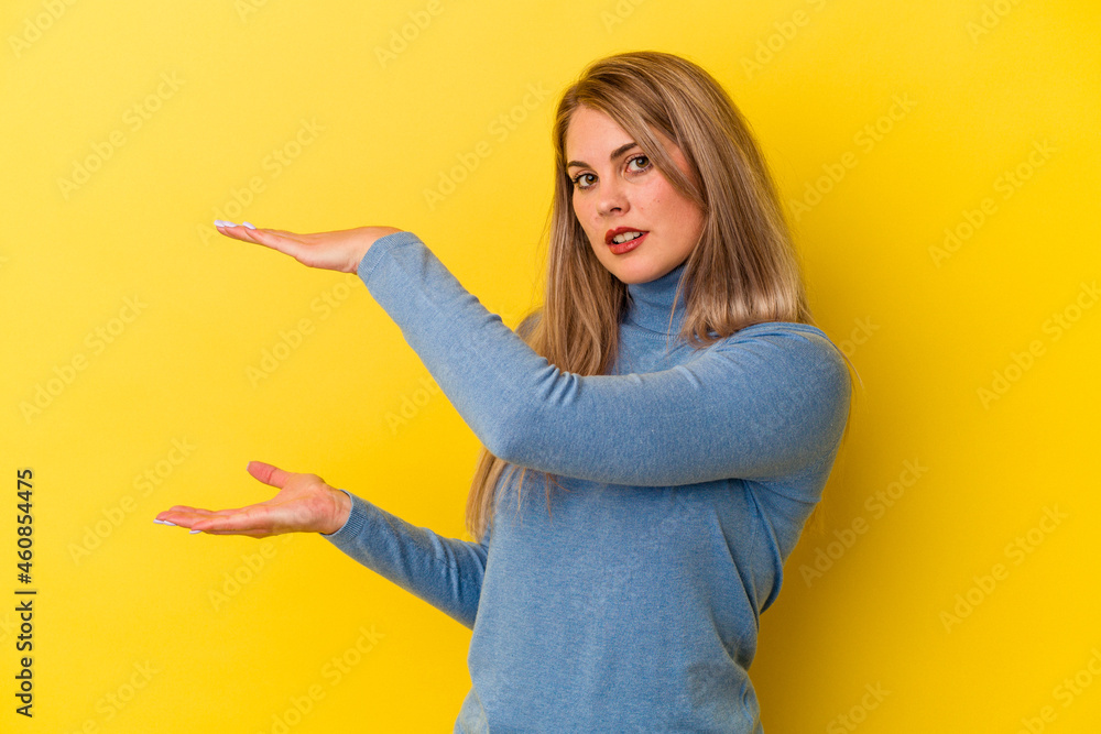 Young russian woman isolated on yellow background holding something with both hands, product presentation. Young russian woman isolated on yellow background holding something with both hands, product presentation.