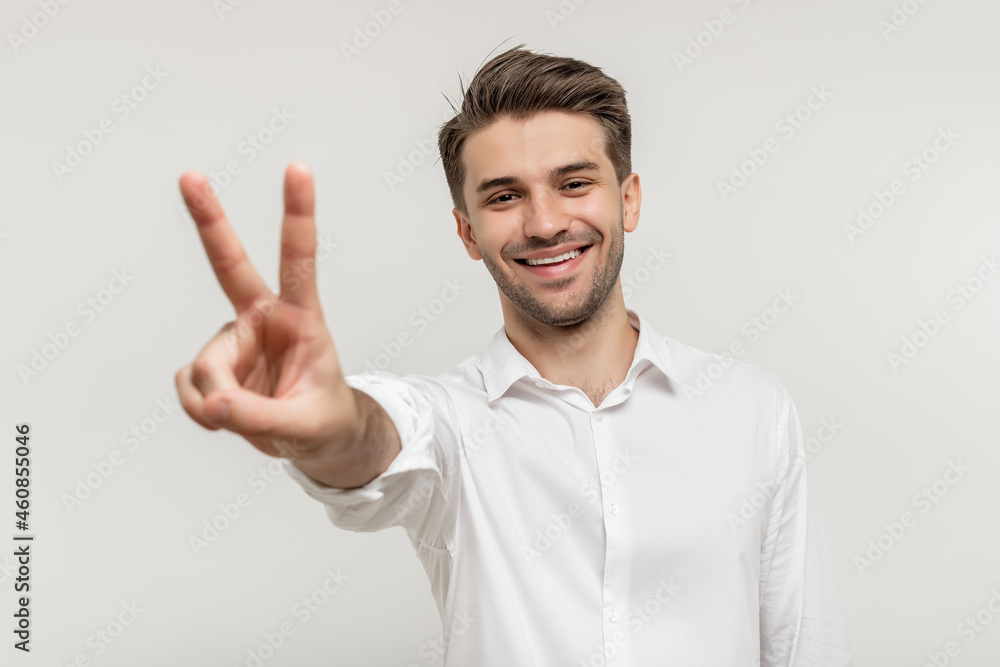 Young happy man with beard wearing white shirt standing over white background smiling and showing two fingers on camera hand doing victory sign. Number two. Young happy man with beard wearing white shirt standing over white background smiling and showing two fingers on camera hand doing victory sign. Number two.