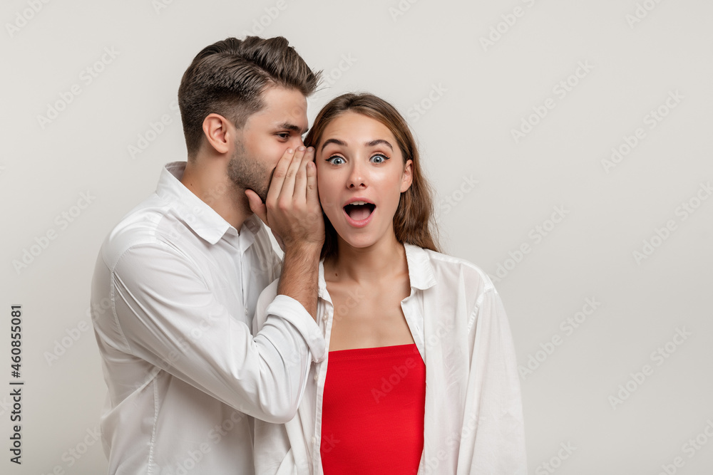Image of handsome young man whispering secret or interesting gossip to shocked beautiful woman in her ear isolated over white background Image of handsome young man whispering secret or interesting gossip to shocked beautiful woman in her ear isolated over white background