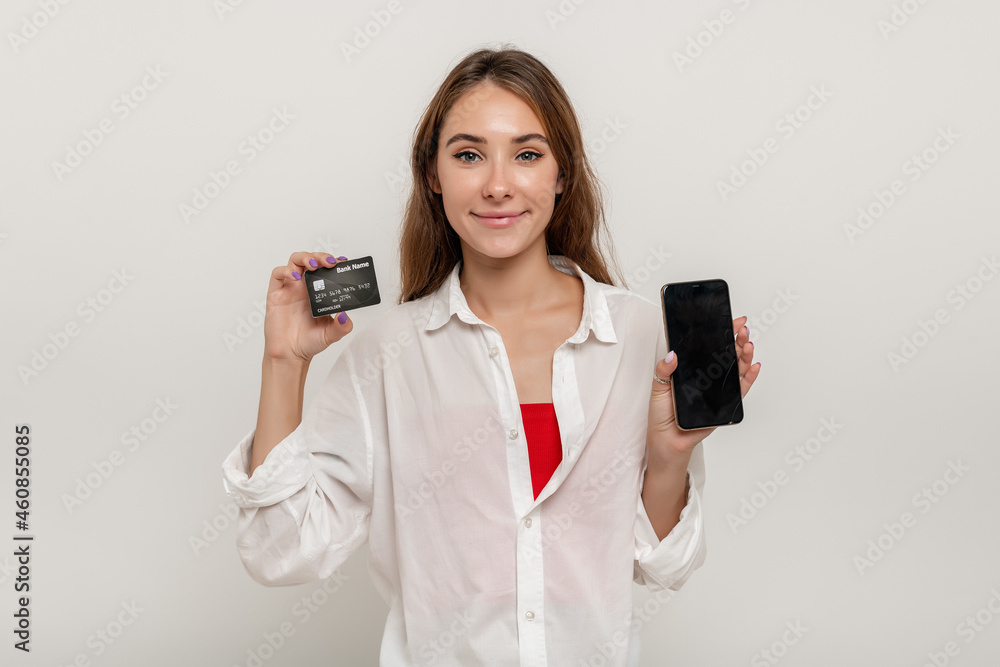 Portrait of a happy young girl showing plastic credit card while holding mobile phone with black screen isolated over yellow background Portrait of a happy young girl showing plastic credit card while holding mobile phone with black screen isolated over yellow background