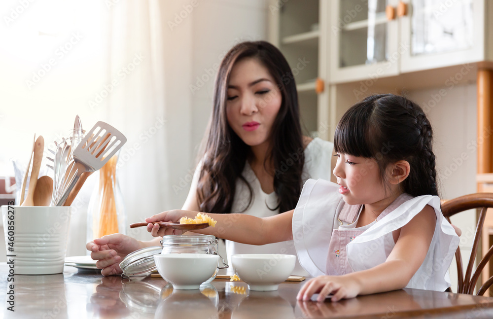 Mom and daughter spend time together at home. Young Asian mother teaches little adorable daughter make breakfast together in the kitchen room at home. Housewife concept.