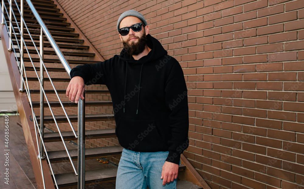 City portrait of handsome hipster guy wearing black blank hoodie with space for your logo or design. Mockup for print. Hoodie template City portrait of handsome hipster guy wearing black blank hoodie with space for your logo or design. Mockup for print. Hoodie template