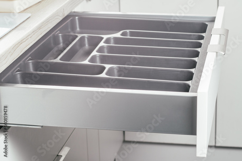 Empty open drawer of white kitchen set with black cutlery organizer tray, side view. Storage organization system © Евгения Рубцова
