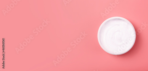 Cosmetic cream banner background. White cosmetic cream for skin and body in an open white jar on a pink empty background. Copy space