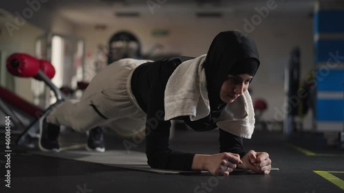 Portrait of endurant Middle Eastern sportswoman in plank position on exercise mat indoors. Concentrated motivated confident woman in hijab exercising working out in gym. Confidence and sport concept photo