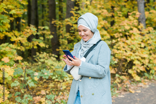 Muslim woman at the park using smartphone connected online wireless. Space for advertisement