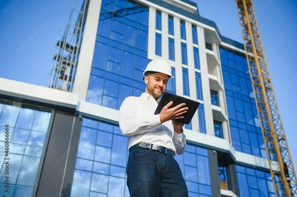 Successful engineer or architect, crane and building construction at backgrpound. Joyous businessman with wearing helmet. Successful engineer or architect, crane and building construction at backgrpound. Joyous businessman with wearing helmet.