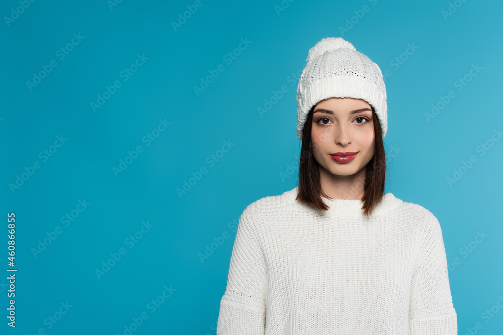 Pretty young woman in white hat and sweater looking at camera isolated on blue Pretty young woman in white hat and sweater looking at camera isolated on blue