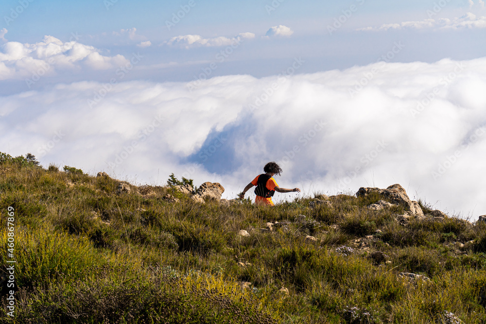 Woman seen from behind, running down the side of a mountain with clouds in the background. 