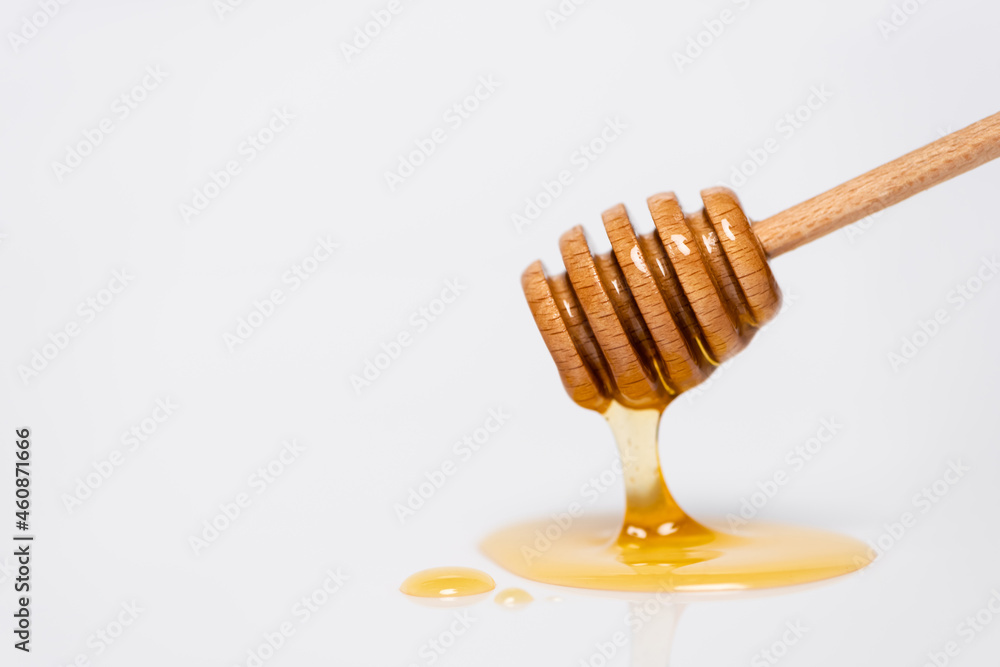 fresh, golden honey flowing from wooden dipper on white background fresh, golden honey flowing from wooden dipper on white background