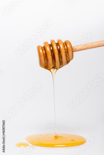 fresh, liquid honey flowing from wooden dipper on white background