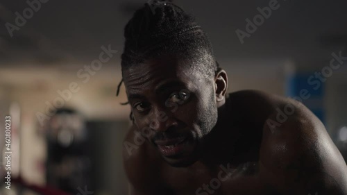 Close-up exhausted tired sportsman breathing standing in gym looking at camera. Portrait of perspiring sweating African American man posing on workout training indoors. Motivation and confidence