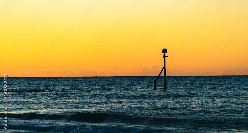 A wooden Groyne standing out of the sea at sunset