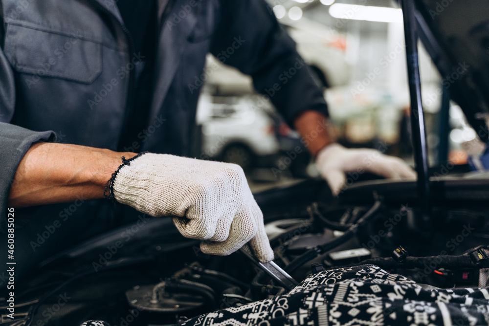 Caucasian male mechanic repairs car in garage. Car maintenance and auto service garage concept. Closeup hand and spanner Caucasian male mechanic repairs car in garage. Car maintenance and auto service garage concept. Closeup hand and spanner