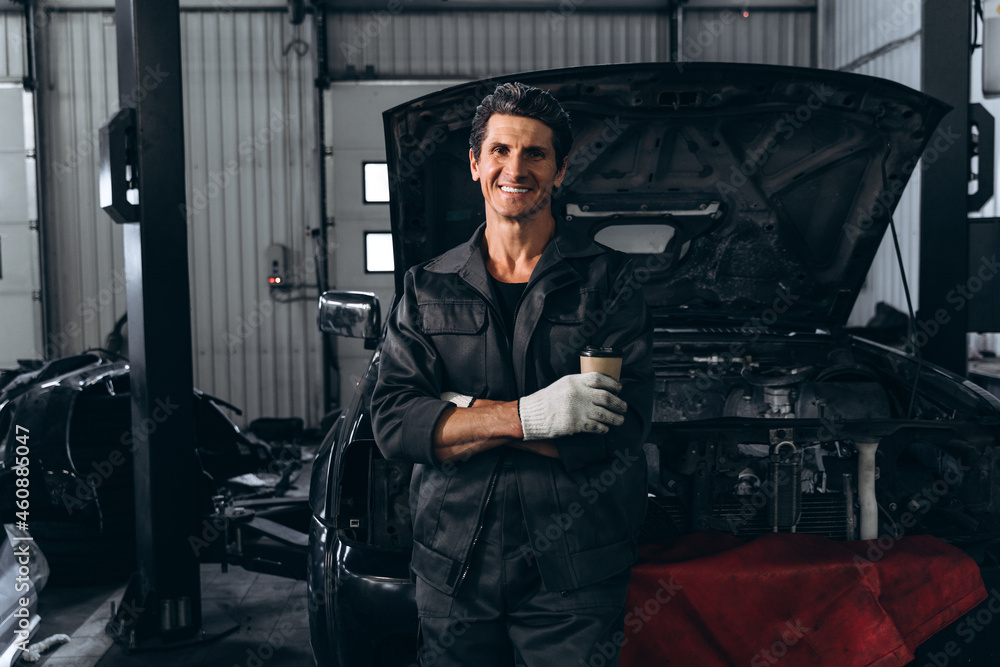 Waist up portrait view of the auto mechanic standing near opened car outdoors and holding wrench. Car repair concept