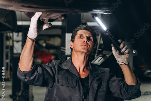 Car service, repair and people concept. Waist up portrait view of the auto mechanic man with lamp working at the workshop