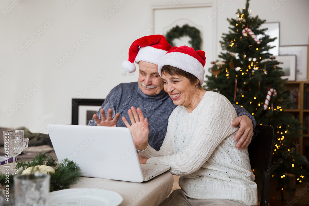 Elderly couple in a Santa's hat using laptop and having video call with friends or relatives at home. Christmas at home Elderly couple in a Santa's hat using laptop and having video call with friends or relatives at home. Christmas at home