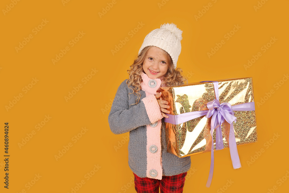 a little happy beautiful blonde girl in a white knitted hat and a knitted gray winter jacket holds a gift box in her hands a little happy beautiful blonde girl in a white knitted hat and a knitted gray winter jacket holds a gift box in her hands