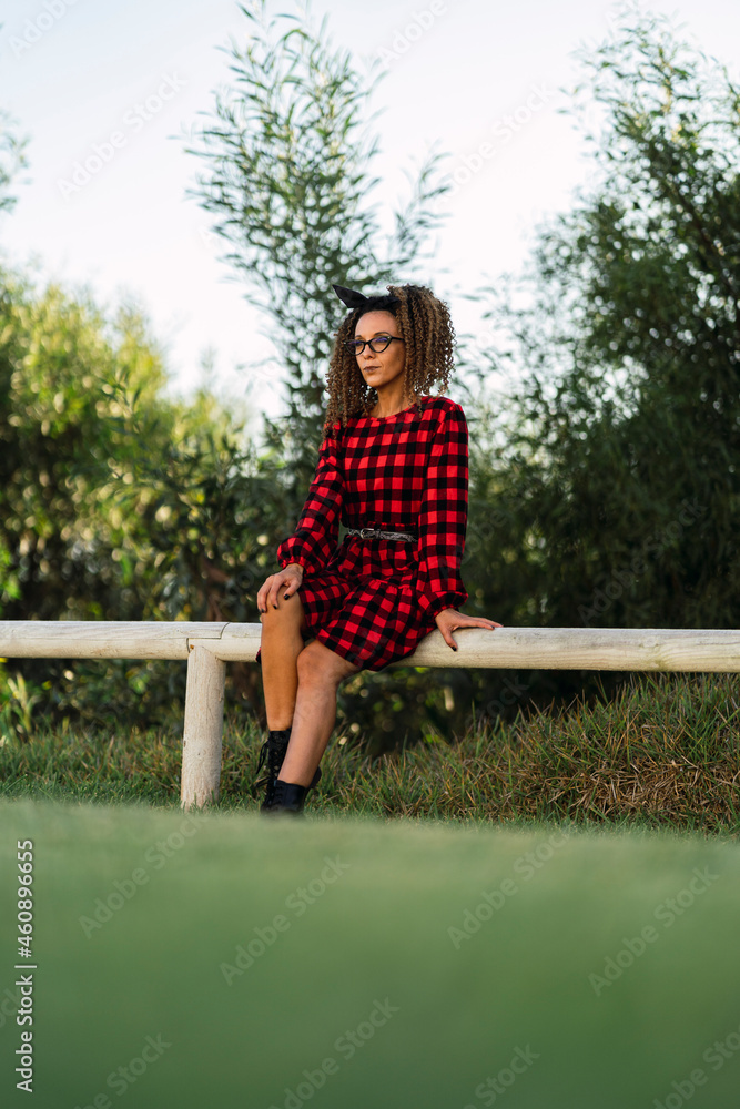 Chica delgada con el pelo rizado y vestido de cuadros rojos y negros en parque posando Chica delgada con el pelo rizado y vestido de cuadros rojos y negros en parque posando