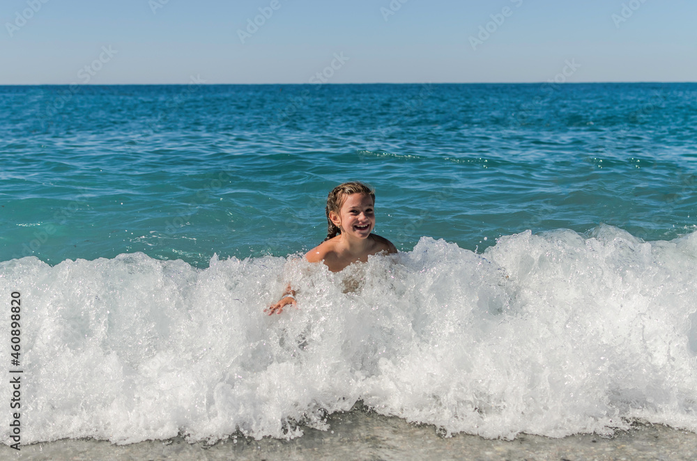 Little happy adorable girl child swims in the sea and plays on the waves during the holidays on the sea coast