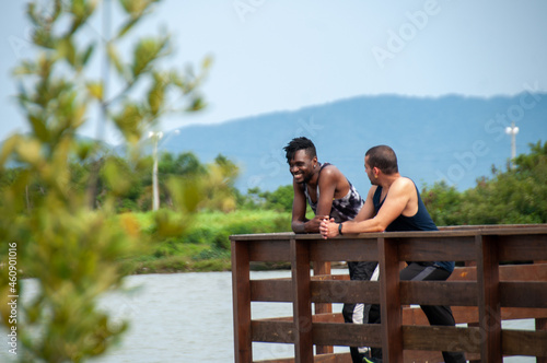 gay couple, black african man, dread in hair talking leaning on bridge over sea in sunny day, walking, healthy life.