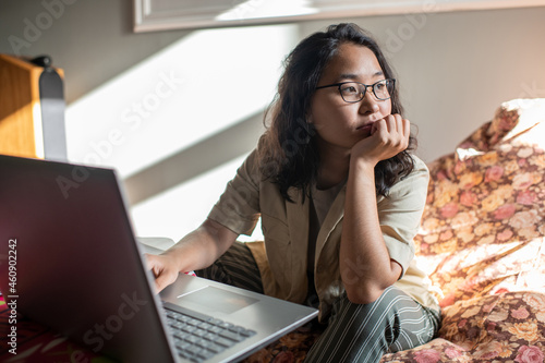 Young distracted female in casualwear and eyeglasses sitting in front of laptop photo