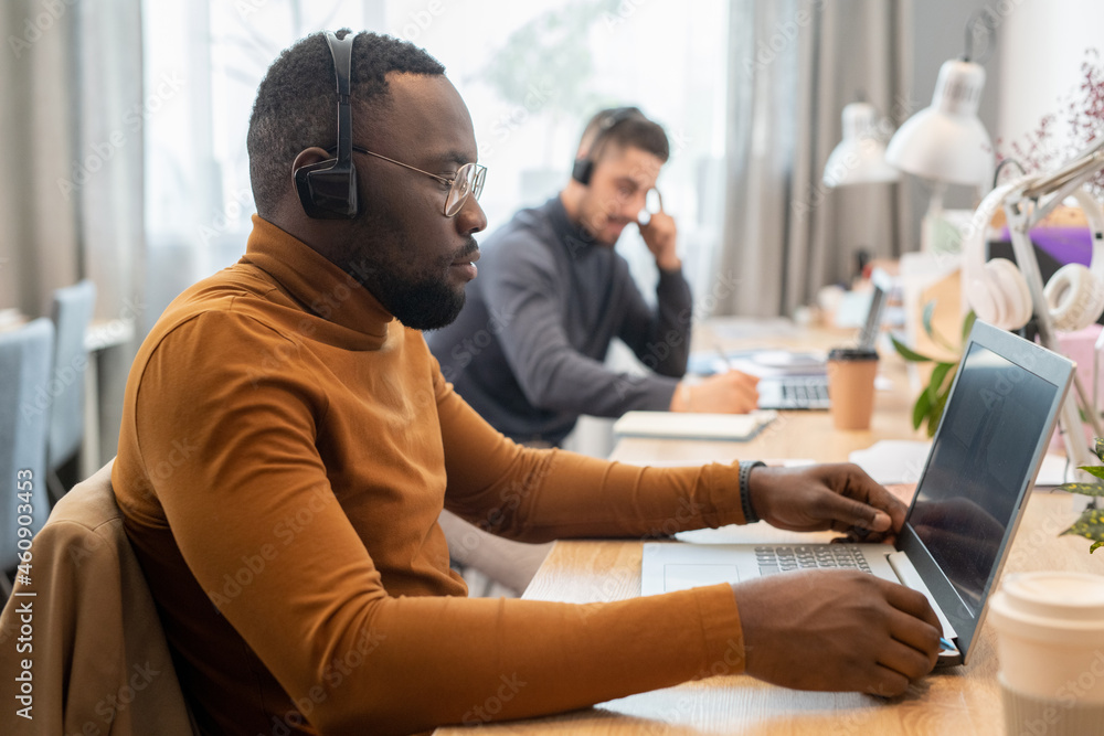 Young serious African man with headset looking at laptop display during online consultation