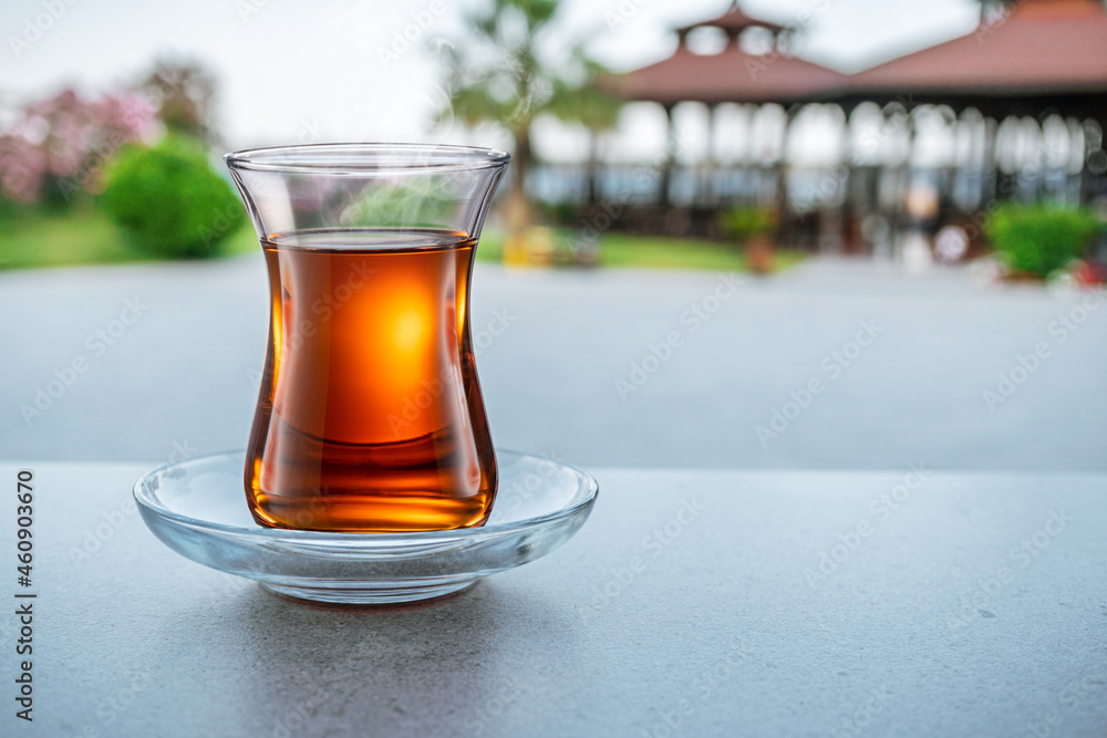 Turkish tea served in tulip-shaped glass on a small saucer blurred nature background. Summer holiday background. Turkish tea served in tulip-shaped glass on a small saucer blurred nature background. Summer holiday background.