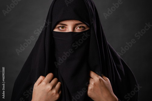 Close up portrait of young, adult woman in black burqa with hidden face, isolated on black background.